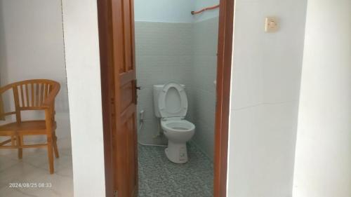 a bathroom with a toilet and a wooden chair at Pondok Sandan Kintamani in Kubupenlokan