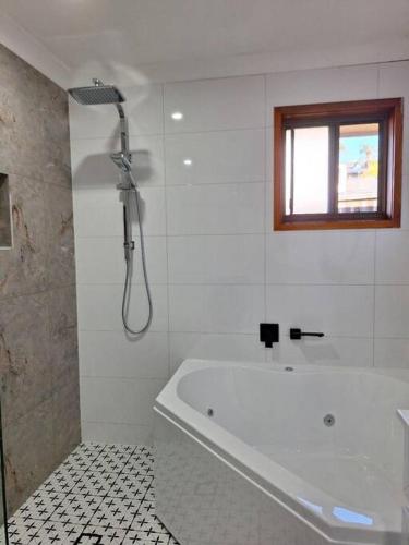 a white bathroom with a tub and a window at Comfy 3 bed house in Ulladulla in Ulladulla