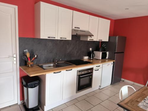 a kitchen with white cabinets and red walls at Les Champs De La Mer in Auberville-la-Renault