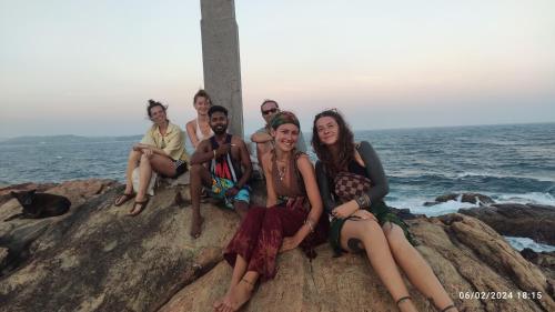 a group of people sitting on a rock by the ocean at Evoke Hostels, Hiriketiya beach in Dickwella