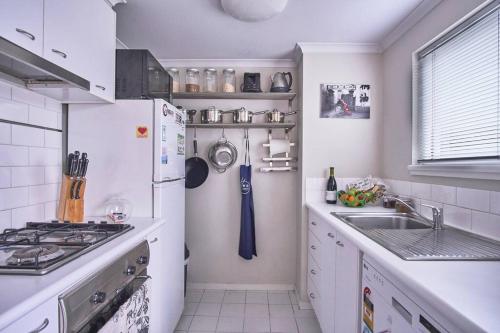 a kitchen with a white refrigerator and a sink at 1BR eco apartment with tennis court and carpark in Melbourne
