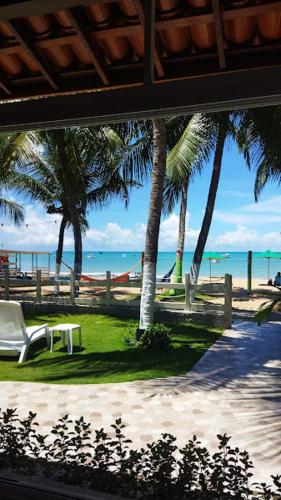 a view of a beach with palm trees and a bench at Pousada Fenícia in Japaratinga