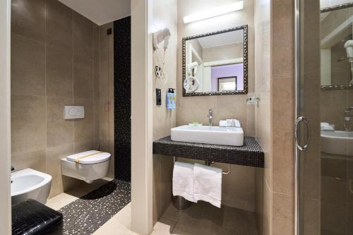 a bathroom with a sink and a toilet and a mirror at Parc Hotel Flora S in Riva del Garda