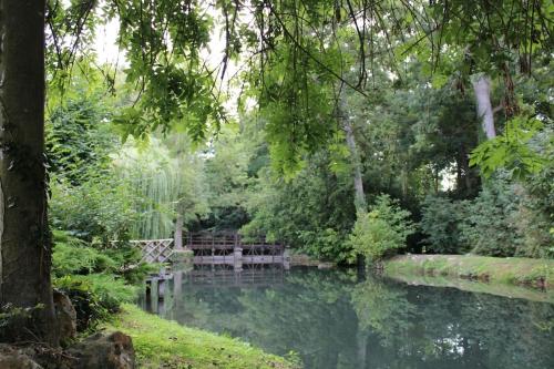 a pond in a park with a bench and trees at Gîte du Moulin rouge in Vernouillet