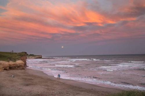 two people walking on the beach at sunset at Hermosa casa de campo a 100 mts del mar in Chapadmalal