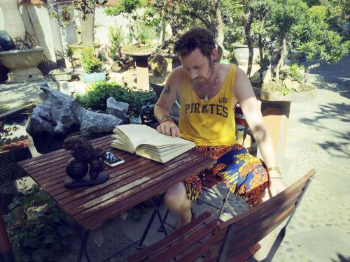 a man sitting on a bench reading a book at Bonsai Villa Hoi An in Hoi An