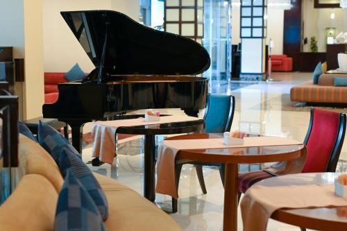 a piano in a room with tables and chairs at City Seasons Hotel & Suites Muscat in Muscat