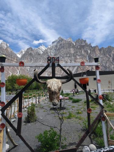 a cow standing behind a fence with mountains in the background at Passu Cones Hotel in Pasu