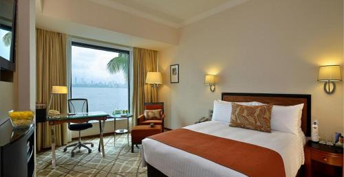 a hotel room with a bed and a desk and a window at Hotel Marine Plaza in Mumbai