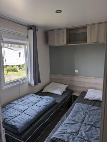 deux lits dans une petite pièce avec une fenêtre dans l'établissement Mobil-home Mick et Stefie, à Saint-Julien-en-Born
