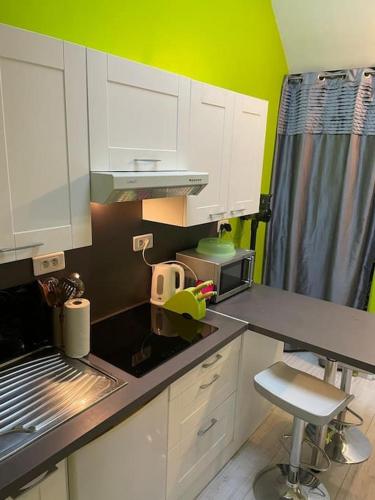 - une cuisine avec des placards blancs et un mur vert dans l'établissement Appartement T3 individuel avec accès piscine et jardin privés, à Basse-Goulaine