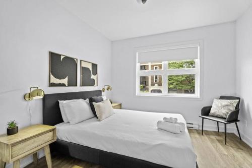 a white bedroom with a large bed and a chair at Stylish 2 Bedroom Haven by Jean Talon Market in Montréal
