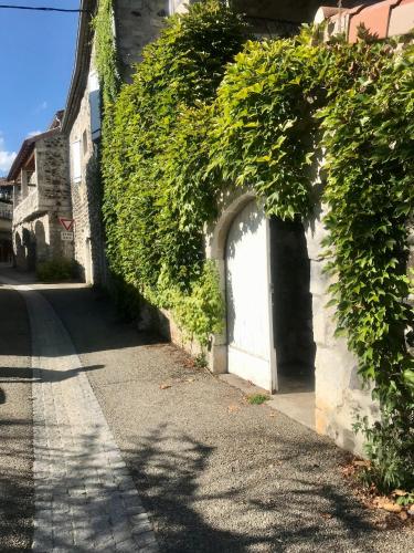 un bâtiment recouvert de lierre avec une porte blanche dans une rue dans l'établissement La Figuiere du village, à Lavilledieu