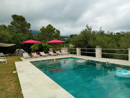 une piscine avec des chaises et des parasols dans l'arrière-cour dans l'établissement Bel appartement indépendant dans un mas provençal, à Tourrettes-sur-Loup