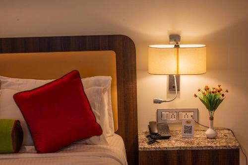 a hotel room with a bed with a red pillow and a lamp at La Oasis by Meraden ,Goa in Anjuna