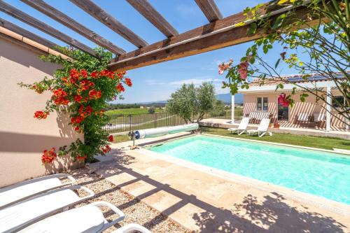 - une piscine avec des chaises blanches et des fleurs rouges à côté d'une maison dans l'établissement Les Terrasses de Cascavelle, à Blauvac