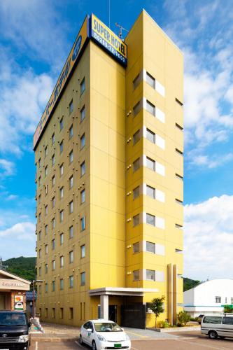a yellow hotel building with cars parked in a parking lot at Super Hotel Arai Niigata in Myoko