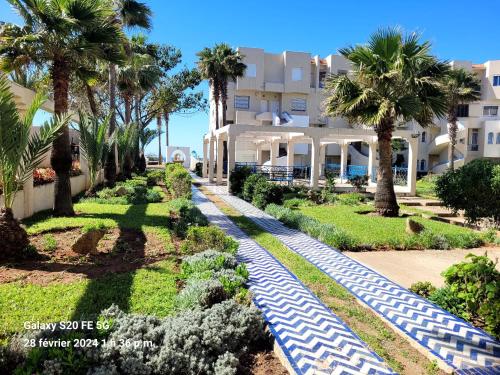 a resort with palm trees in front of a building at Cosy appartement sur la plage in Jbila
