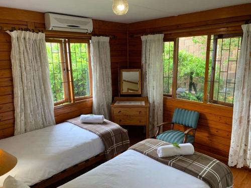 a bedroom with two beds and a chair and windows at Bay View Cabin in Gordonʼs Bay