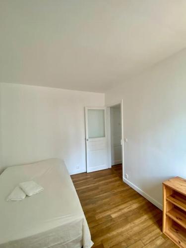 une chambre blanche avec un lit et un parquet dans l'établissement Appartement - Proche Paris - Stade de France, à Saint-Denis