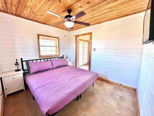 Un dormitorio con una cama morada y un ventilador de techo. en Little Haus on the Farm with a Hot Tub, en Fredericksburg