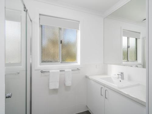 a white bathroom with a shower and a sink at Painters Island Holiday Park in Wangaratta