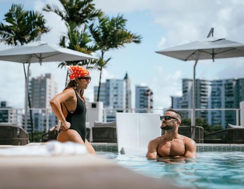 a man and a woman sitting in a swimming pool at Hilton Garden Inn San Juan Condado in San Juan