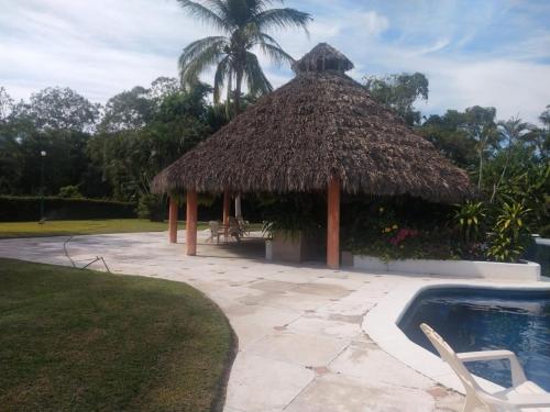 a pavilion with a straw hut and a swimming pool at Habitaciones con baño privado en Departamento compartido en Club Santiago Manzanillo in Manzanillo