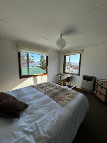 a bedroom with a large white bed and two windows at Hostal Amerindia in Puerto Natales