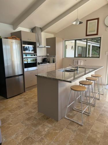a kitchen with a island with bar stools and a refrigerator at Water's Edge Holiday Home in Opua