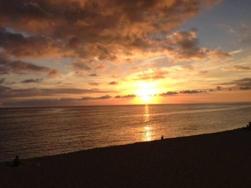 a sunset on the beach with people on the beach at Valley Vibes and Beach Bliss Condo for Family Nomads in Waianae