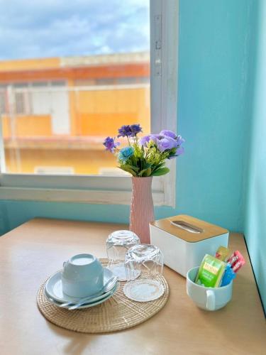 a table with a vase with purple flowers and glasses at Ocean Blue Huahin Guesthouse in Hua Hin