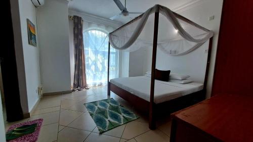 ein Schlafzimmer mit Himmelbett und Fenster in der Unterkunft Ary Homestay - On 5th Avenue in Nyali