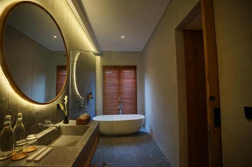 a bathroom with a tub and a large mirror at The Shanti Graha Villas in Ubud