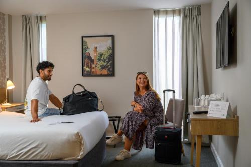 a man and a woman sitting on a bed in a hotel room at Edgbaston Park Hotel Birmingham in Birmingham