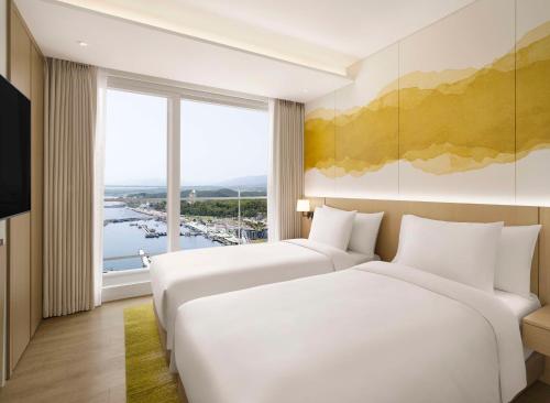 two beds in a hotel room with a large window at Cassia Sokcho in Sokcho