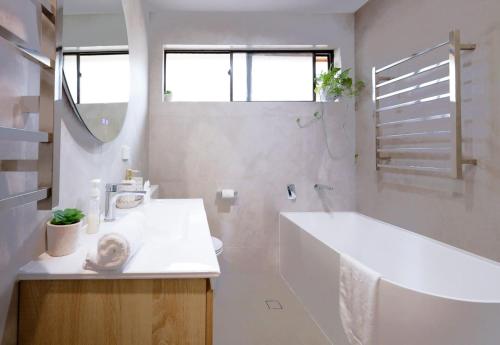 a white bathroom with a tub and a sink at Seaside Haven Tranquil Beachside Escape in Warriewood