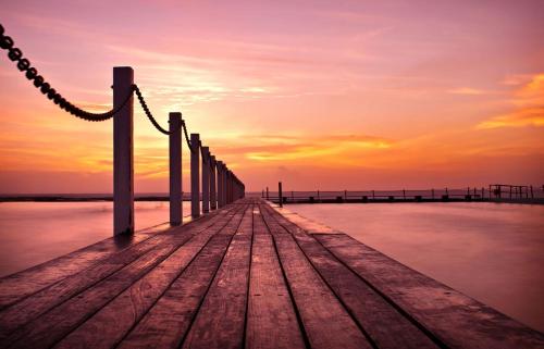 a wooden pier with a sunset in the background at Seaside Haven Tranquil Beachside Escape in Warriewood