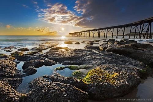a pier on a beach with rocks and the ocean at The Emerald Bower in Rathmines
