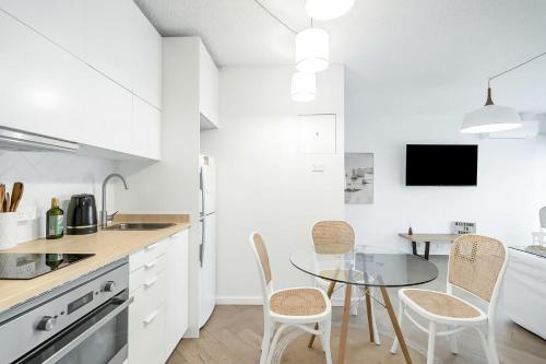 a white kitchen with a glass table and chairs at The Little Bondi Base in Sydney