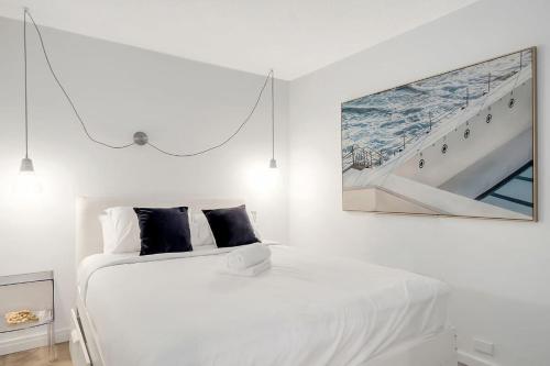 a white bedroom with a bed with a picture on the wall at The Little Bondi Base in Sydney