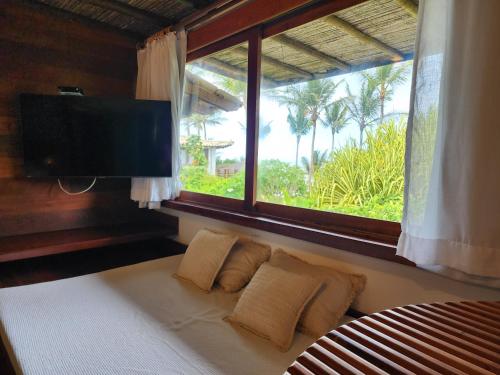 a bedroom with a bed with a window and a flat screen tv at Pousada Vila do Mar in Caraíva