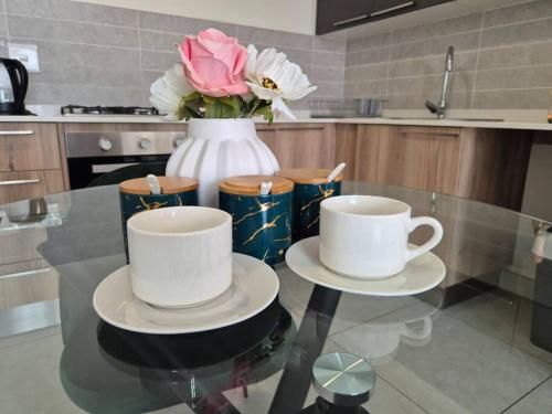 a glass table with two cups and a vase with flowers at Tetani's Luxury Oasis in Lakeside