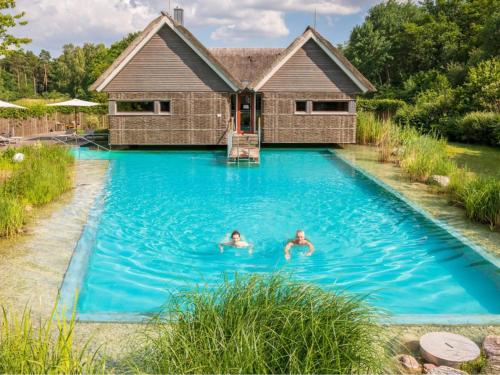 two people swimming in a pool in front of a house at Apartment Beech Resort Plauer See by Interhome in Ganzlin