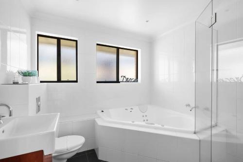 a white bathroom with a tub and a sink and a toilet at Dream View Steps from the Beach in Sydney