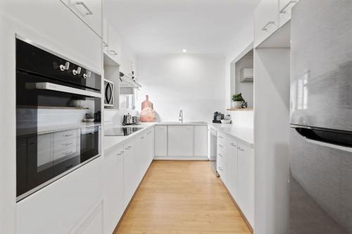 a white kitchen with white cabinets and a wooden floor at Wine Down Retreat - The Great Entertainer with Heated Pool, Fireplace and Firepit for the Perfect All-Season Escape in Cessnock