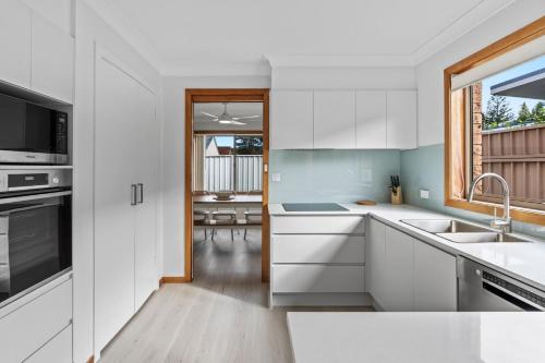 a kitchen with white cabinets and a window at Shoreline Retreat 900m to the beach in Fingal Bay