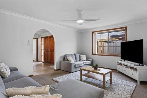 a living room with a couch and a tv at Shoreline Retreat 900m to the beach in Fingal Bay