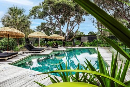 an outdoor pool with chairs and umbrellas at Privately Managed Villa 12 Bangalay Luxury Villas in Shoalhaven Heads