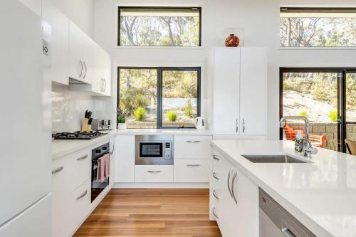 a white kitchen with white counters and windows at Majestic Mountain View in Katoomba in Katoomba